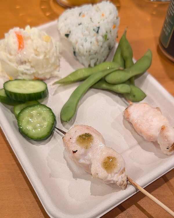 Breast and tender skewers along with onigiri, edamame, pickles and potato salad on a plate