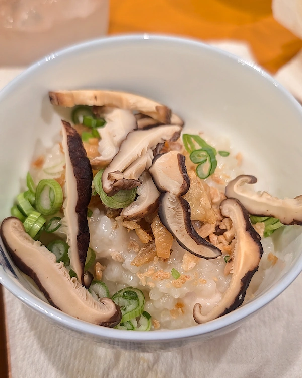 A bowl of chicken congee with chicken breast, skin, garlic and shiitake on top