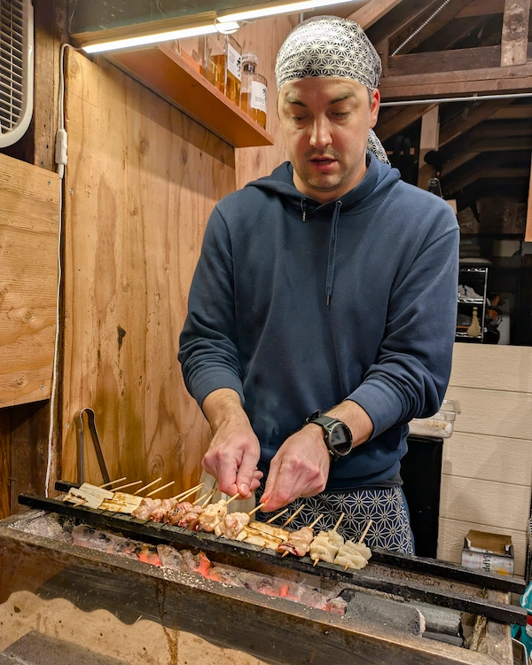 A man rotating skewers on a japanese style charcoal grill